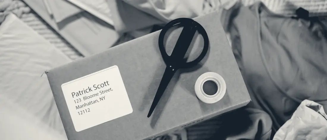 A taped shipping box with an address label, scissors and a roll of tape on top